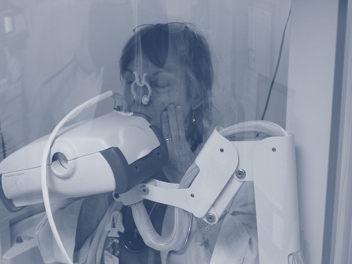 A patient wearing a nose clip, breathing through a mouthpiece inside a glass body box